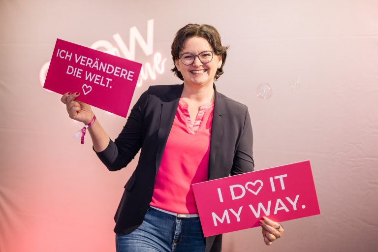 Person posiert vor der Grow & Shine Fotowand mit Spruchschildern